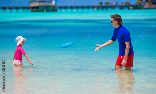 Father and little girl  playing with flying disk at shallow water on the beach