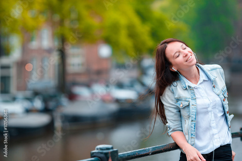 Young beautiful woman listening to music background of canal in Amsterdam, Netherlands © travnikovstudio