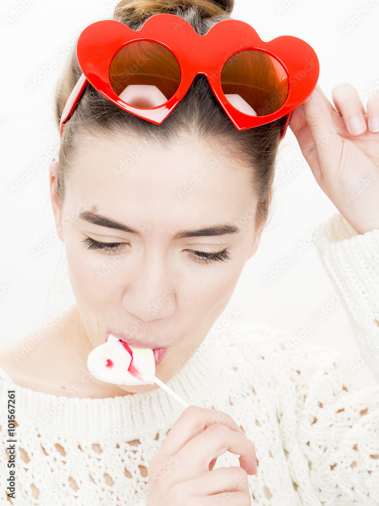 Φωτογραφία Portrait of a young woman with a lollipop and red heart shaped glasses