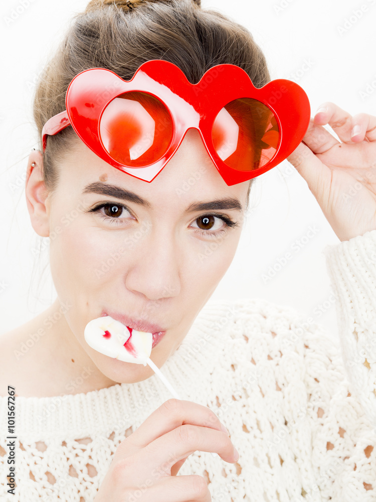 Φωτογραφία Portrait of a young woman with a lollipop and red heart shaped glasses