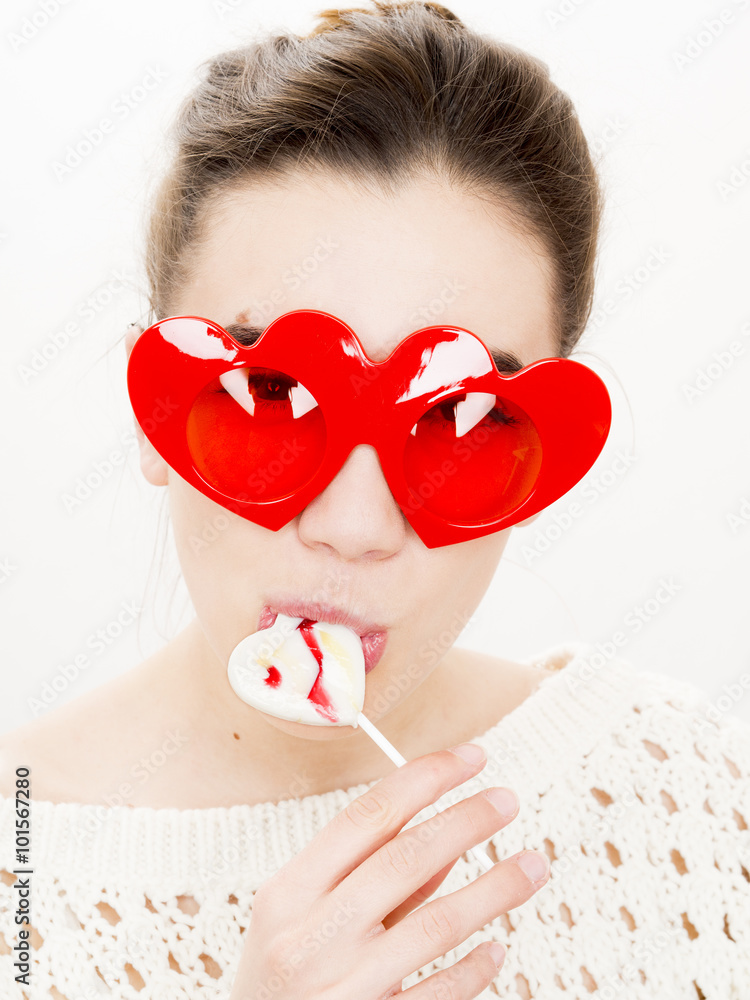 Φωτογραφία Portrait of a young woman with a lollipop and red heart shaped glasses