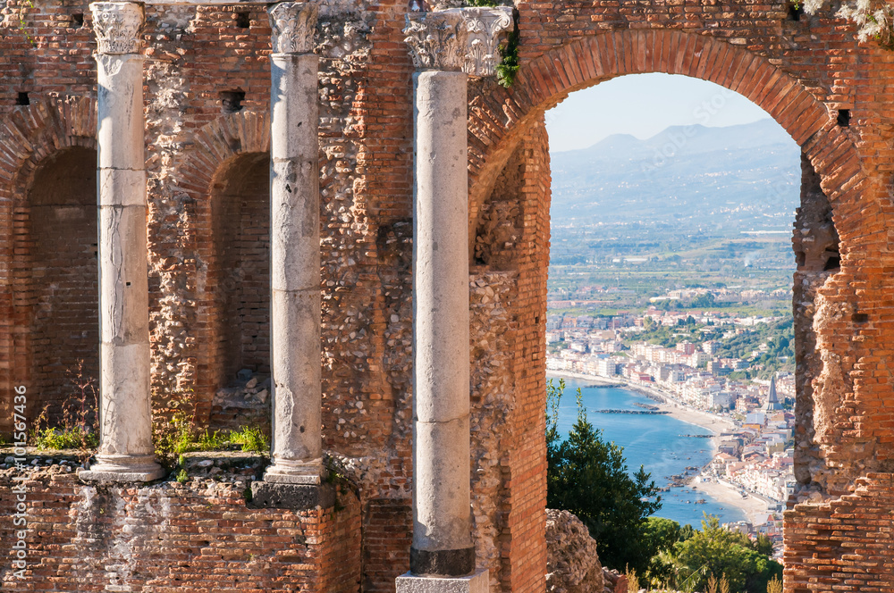 View of some columns and one arch in the scene of the greek theater in Taormina and a perspective of Giardini Naxos in the background