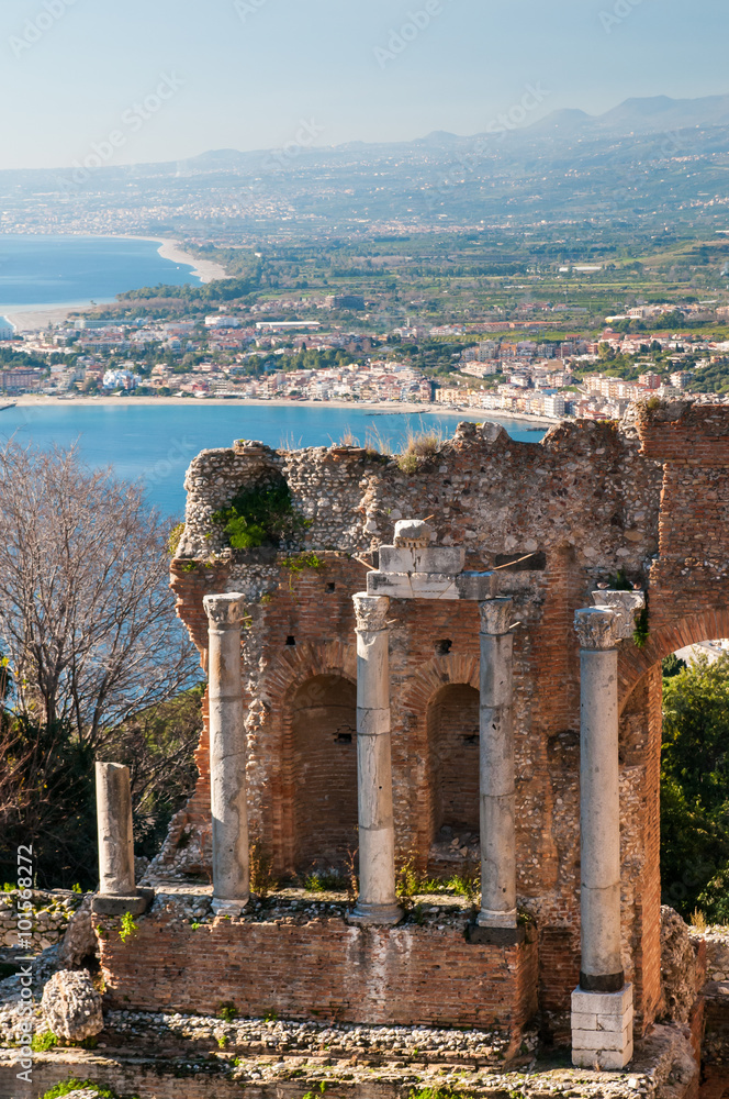 View of some columns in the scene of the greek theater in Taormina and a perspective of Giardini Naxos in the background