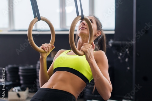 Athlete fit woman exercising in gym pulling up on gymnastic rings.