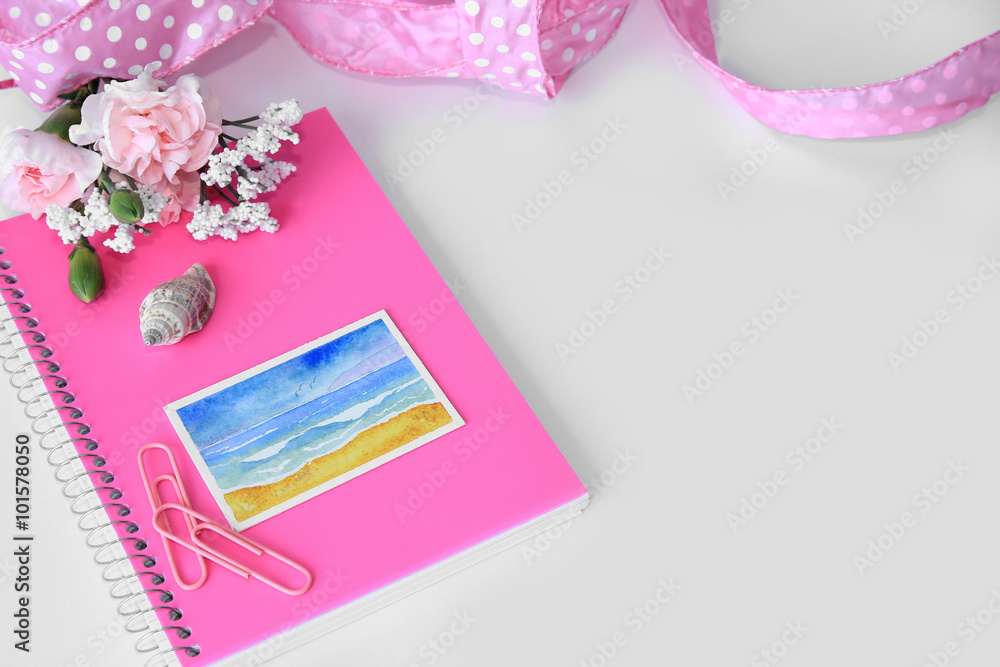 A white background styled desktop with pink paper clips, journal, notebook, ribbon, flowers, and a seashell. A white background styled desktop with pink paper clips, journal, notebook, ribbon, flowers, and a seashell.