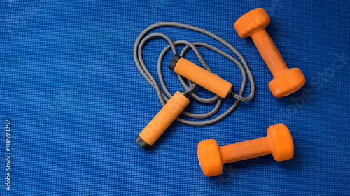 Obraz na plátně Pair of orange dumbbells and jumping rope on blue yoga mat background
