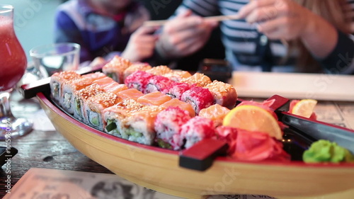 Big set on sushi and rolls on the reastaurant plate, family with child on background
 photo