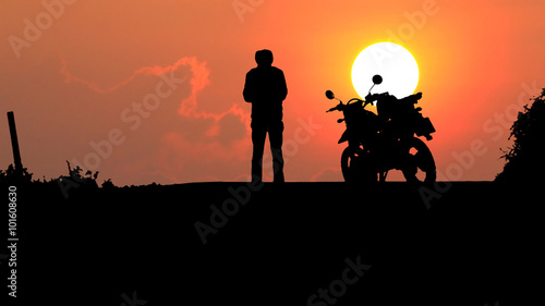 A man and motorcycle over sunset.
