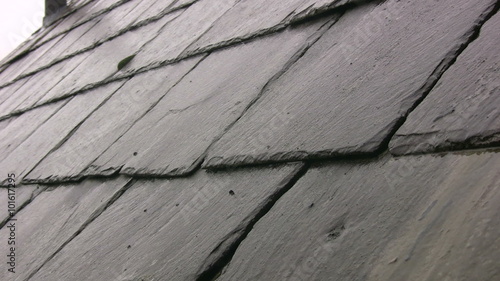 Roof level shot of a slate roof on a Victorian building in the English lake district. A gentle but persistent rain is falling and the water is dripping and running off the roof towards the guttering.