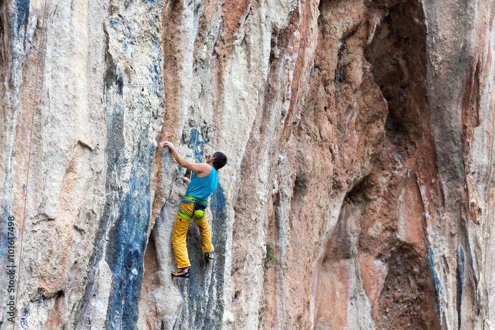 Fototapeta premium Mature Rock Climber ascending steep colorful rocky Wall Lead Climbing