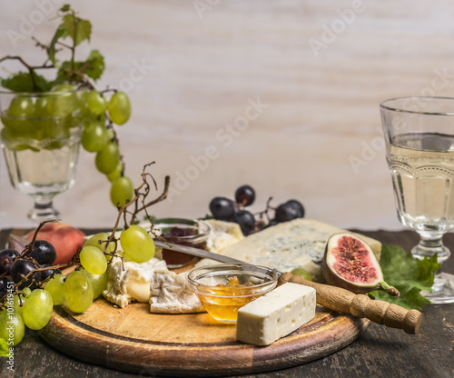 Camembert, Dor Blue, Gorgonzola, honey, grapes and wine on a cutting board on wooden rustic background top view close up