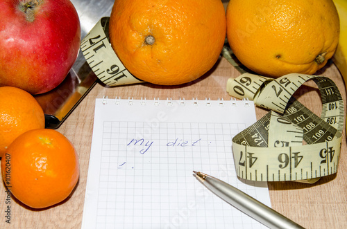 Diet concept with fruit, notebook and measuring tape on wooden table