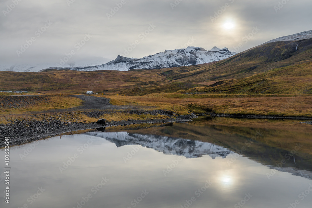View of snow mountain range reflecting on mirror lake in cloudy day autumn season Iceland