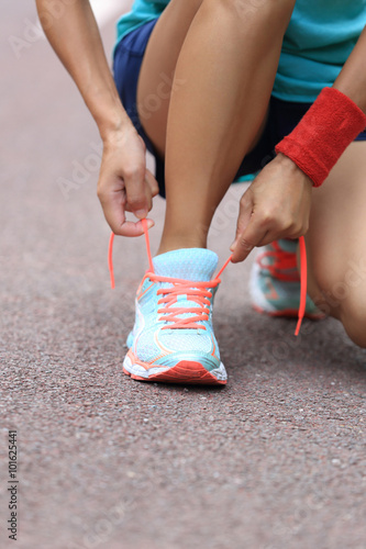 young woman runner tying shoelaces on trail