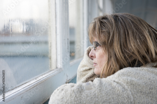 Schilderij op canvas Portrait image of a fed up mature woman looking out of the window on a rainy mis