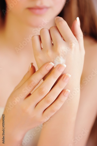 Young woman applies cream on her hands after bath. Focus on hand