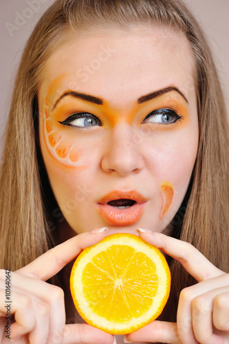 Young beautiful woman with creative orange makeup with orange in her hands