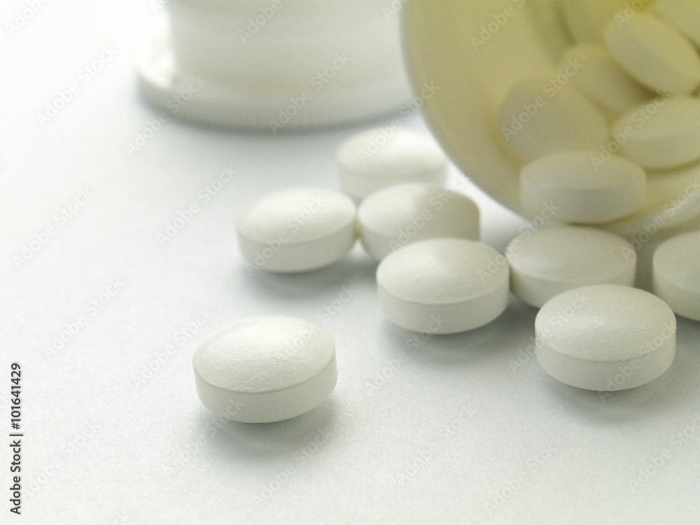 A white pill macro in front of spilled ones and bottle A white pill macro in front of spilled ones and bottle
