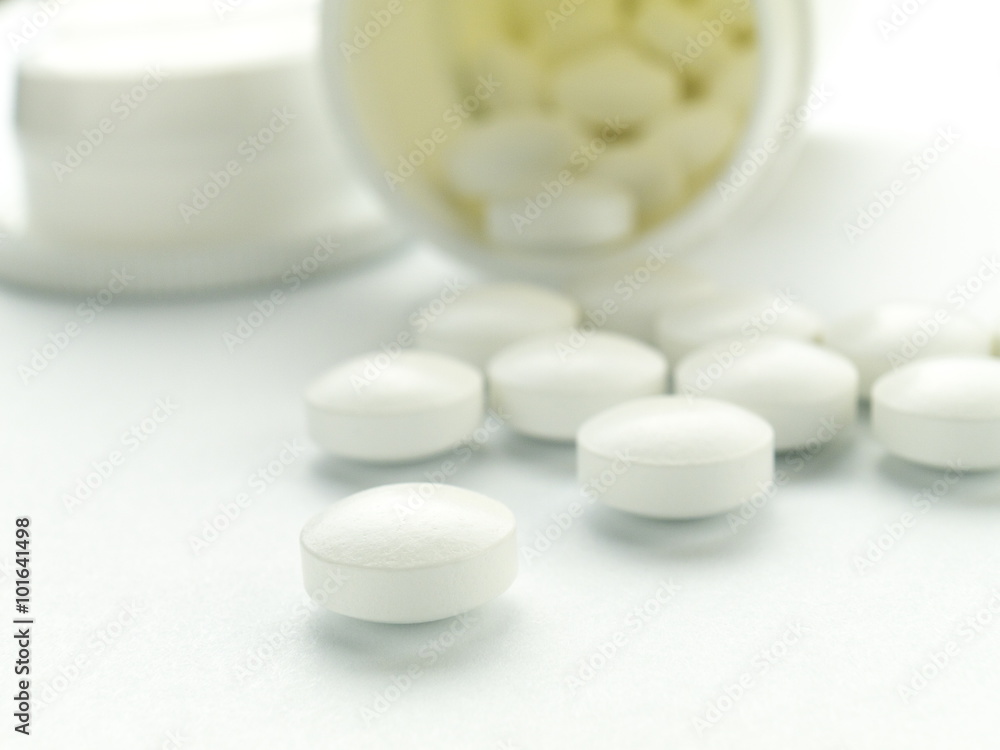 A white pill macro in front of spilled ones and bottle A white pill macro in front of spilled ones and bottle
