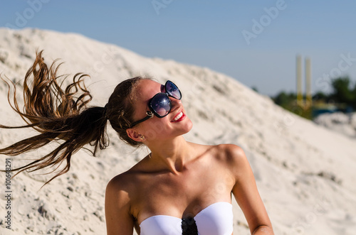 Красивая загорелая девушка брюнетка летом на пляже в черном купальнике и развивающимися волосами