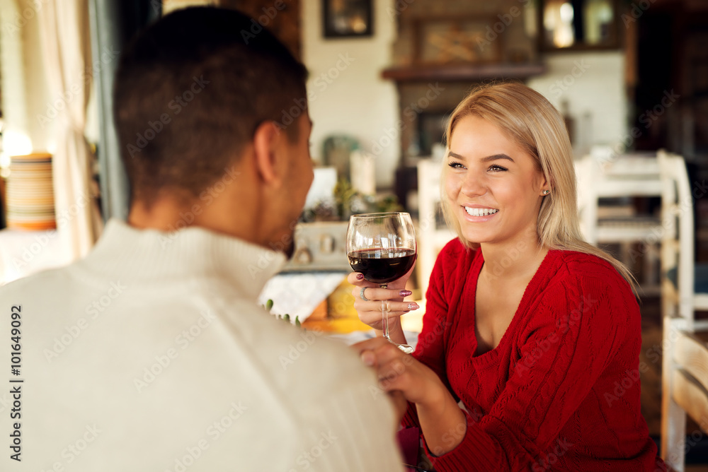 Lovely couple sitting at restaurant and holding hands.She is holding wine glass and looking at him. Shallow depth of field.