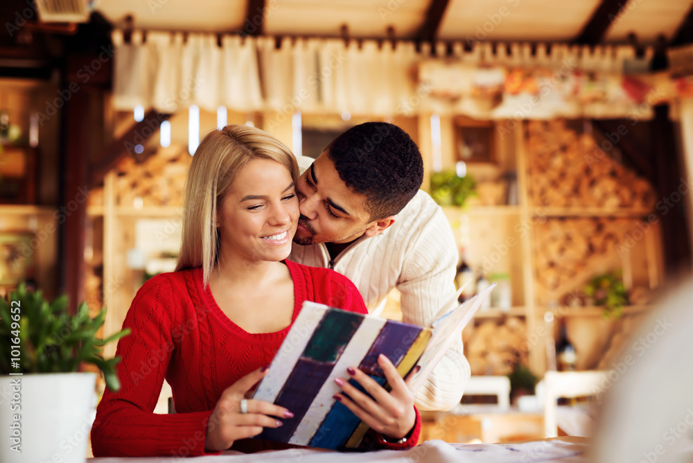 Lovely couple choosing some specialty from menu, while he is kissing her. Shallow depth of field. Lovely couple choosing some specialty from menu, while he is kissing her. Shallow depth of field.