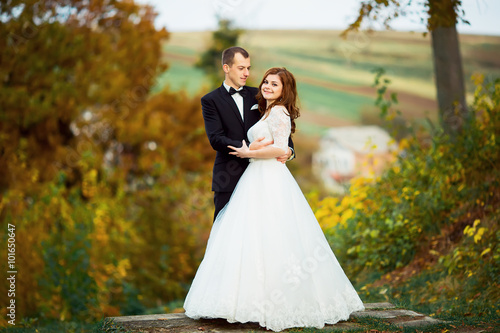 close-up portrait of wedding couples in love hipsters bride in a white dress with flowers and groom in a suit with glasses and bow tie smiling posing touching embrace on a background of autumn forest