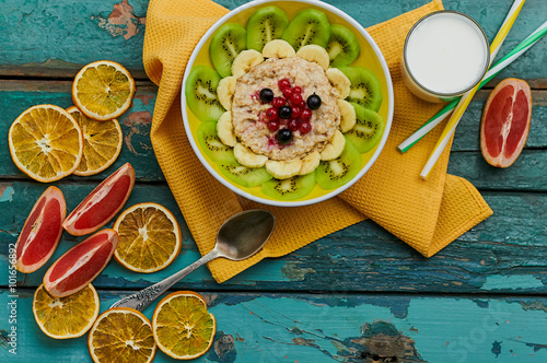 Healthy breakfast with oatmeal and fruit. Granola with kiwi, bananas, berries, grapefruit and a glass of milk. Wooden background. Top view. Selective focus