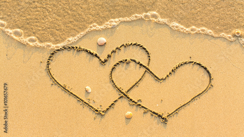 Two hearts drawn on the sand beach with the soft wave. Honeymoon concept.
