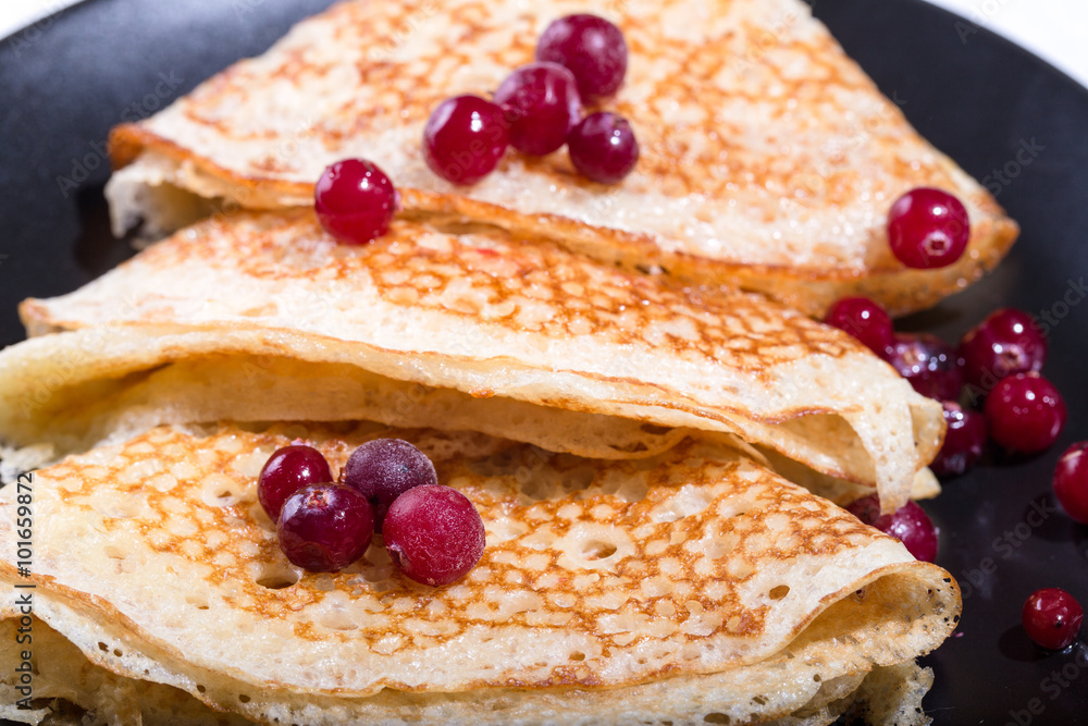 Fragment of a pile of pancakes on a black plate with red berries
