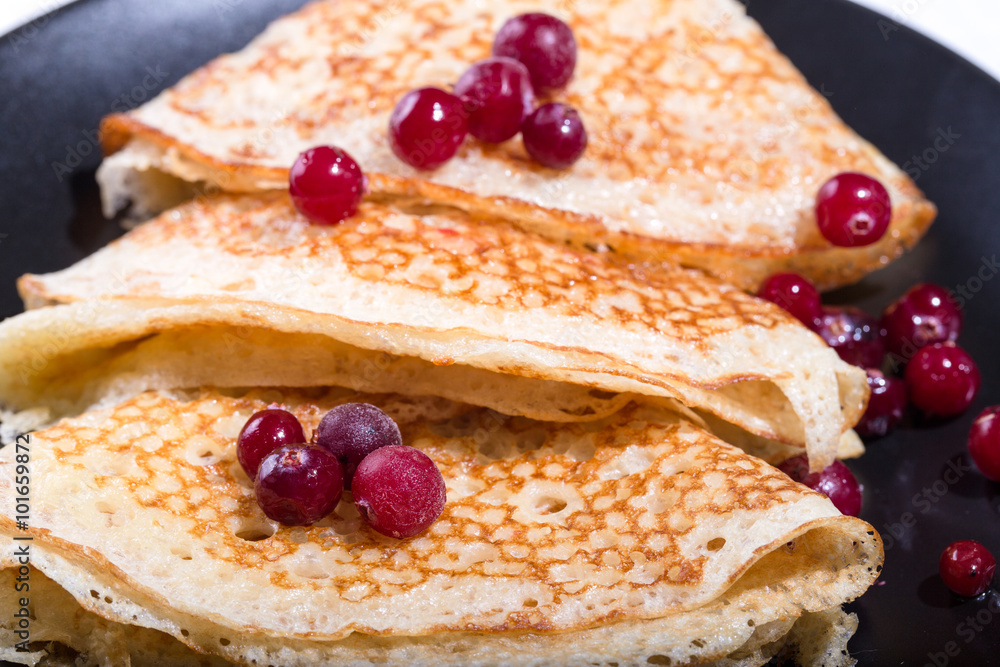 Fragment of a pile of pancakes on a black plate with red berries Fragment of a pile of pancakes on a black plate with red berries