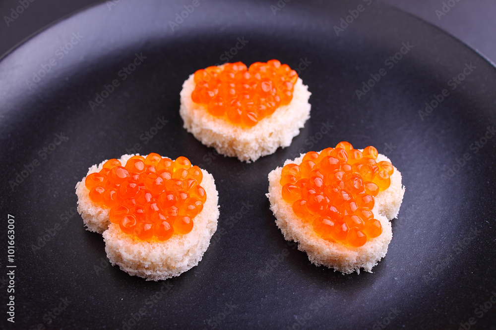 sandwich with red caviar in a heart shape on a black plate sandwich with red caviar in a heart shape on a black plate