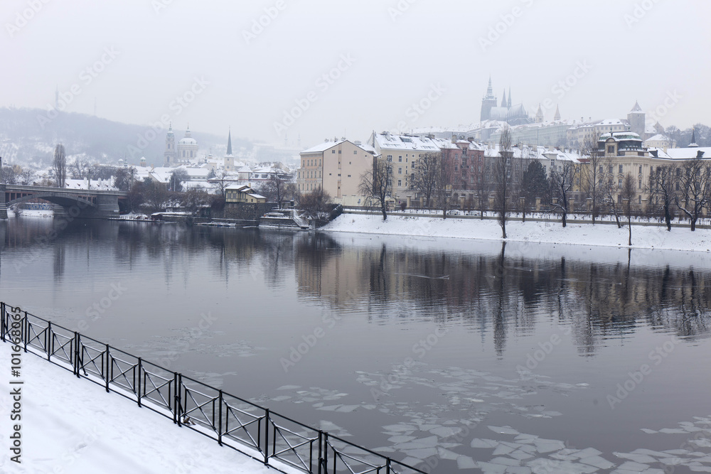 Snowy and foggy Prague Lesser Town with gothic Castle above river Vltava, Czech Republic