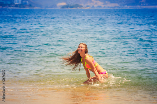 blonde slim gymnast in bikini squats smiles in azure sea