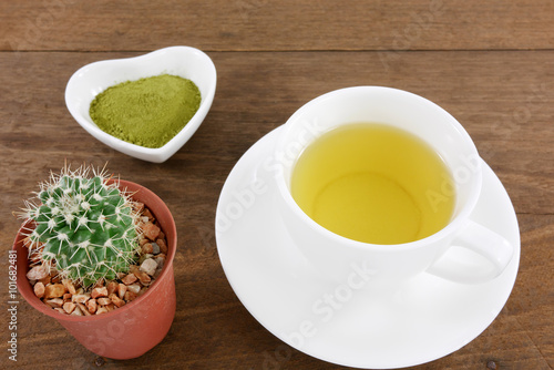 The Japanese matcha green tea powder on ceramic heart shaped bowl and cup of hot green tea and little cactus in plant pot on wooden planks.