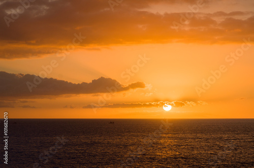 Sunset at ocean, sun partly hidden by clouds