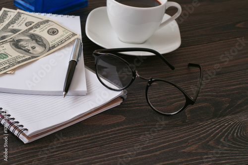 Notebook with glasses, coffee and dollars