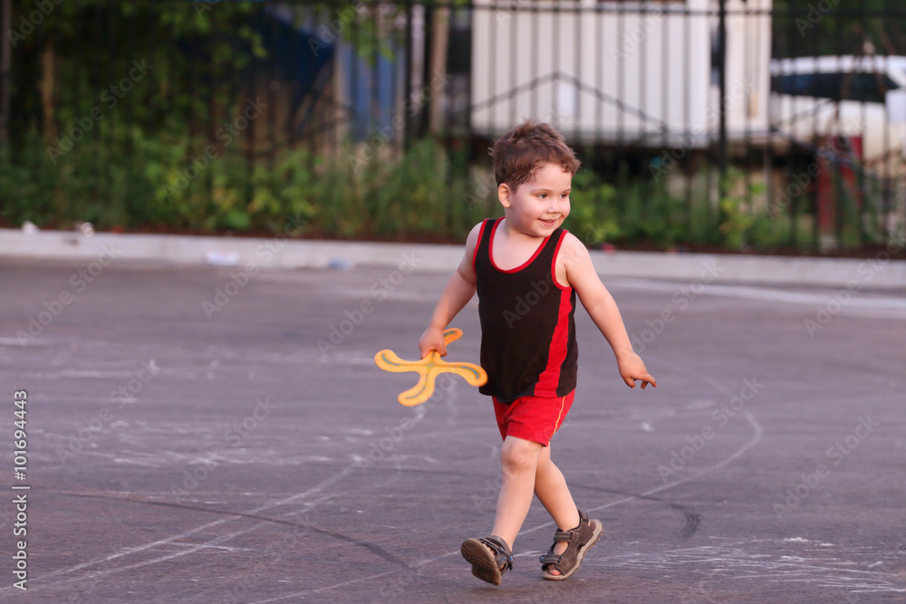 Happy little handsome boy with boomerang runs in summer evening