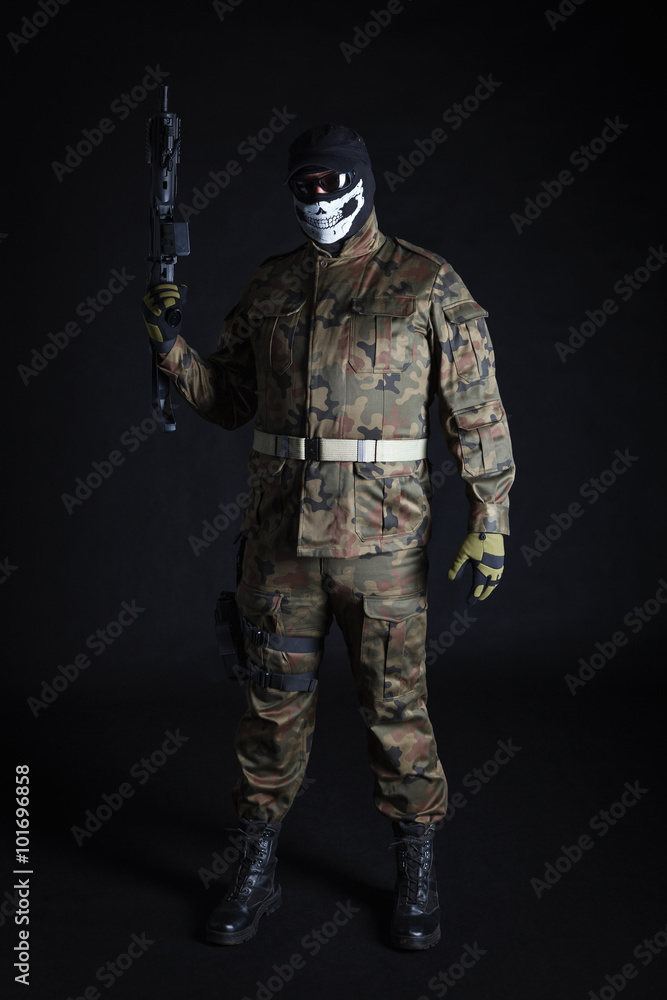 Anti terrorist dressed in camouflage, standing with a gun, looking at camera