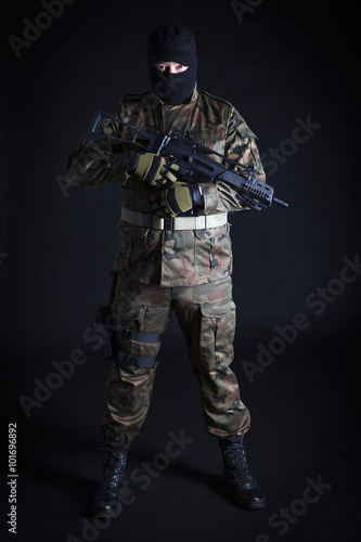 Anti terrorist dressed in camouflage, standing with a gun, looking at camera