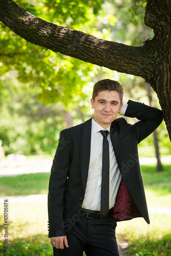 Man dressed suit stands nearthe tree photo