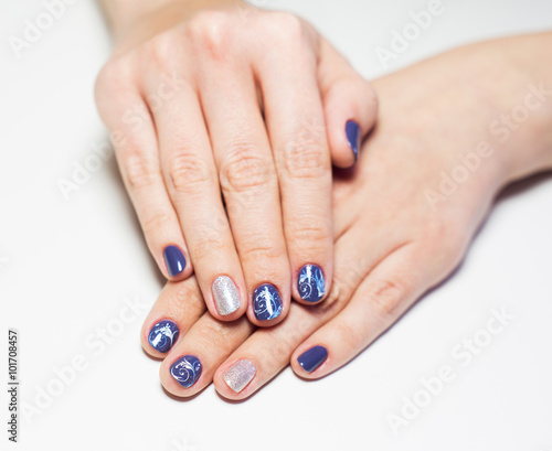 Close up of female hands with professional blue and silver manicure isolated on white background. Art stamping on nails. Modern gel polish with base coat first and top cure with UV or LED lamp.