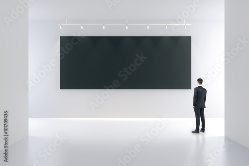 Blank black poster and businessman in white empty room, mock up