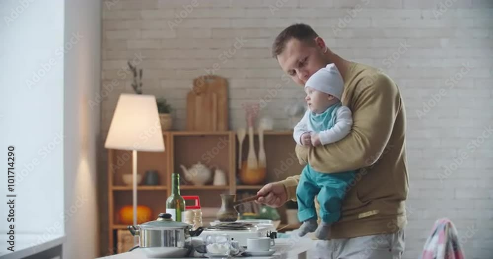 Father holding his lovely baby boy and making morning coffee Father holding his lovely baby boy and making morning coffee