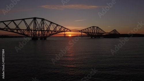 Stunning aerial shot of the Forth Rail Bridge during sunset in South Queensferry with a local train passing
