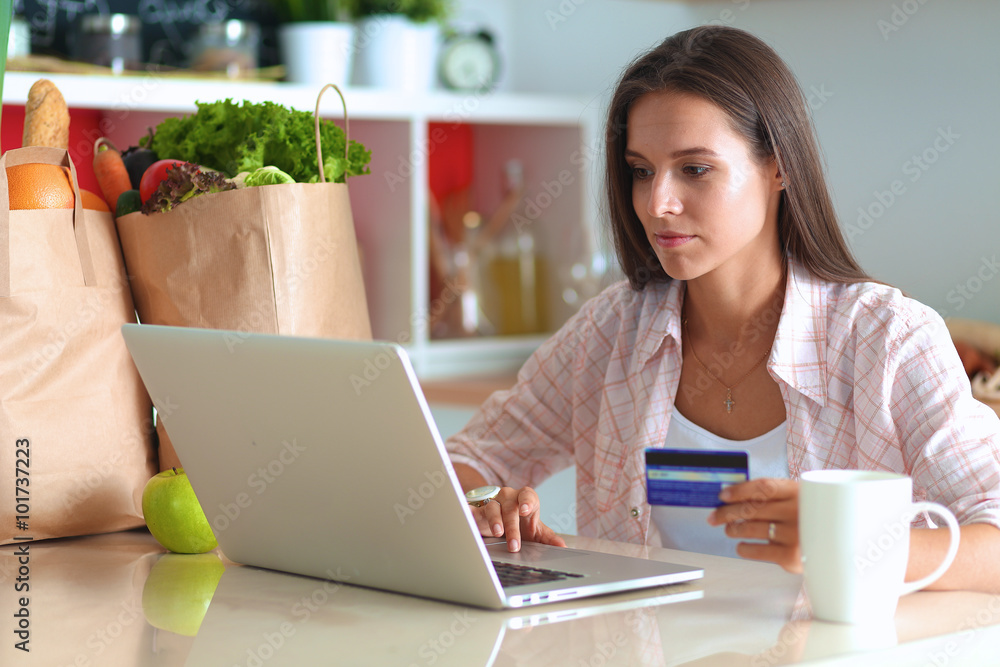 Smiling woman online shopping using tablet and credit card in kitchen Smiling woman online shopping using tablet and credit card in kitchen