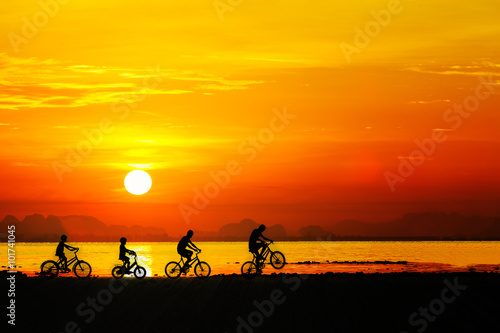 Silhouettes of childrens on bicycle against sunset sky at the be