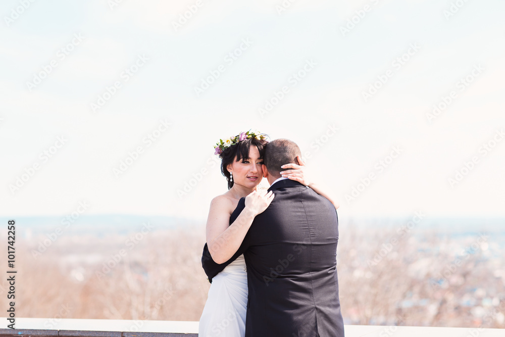 Beautiful elegant young wedding couple is embracing at top of hill with picturesque amazing view at summer bright sky
