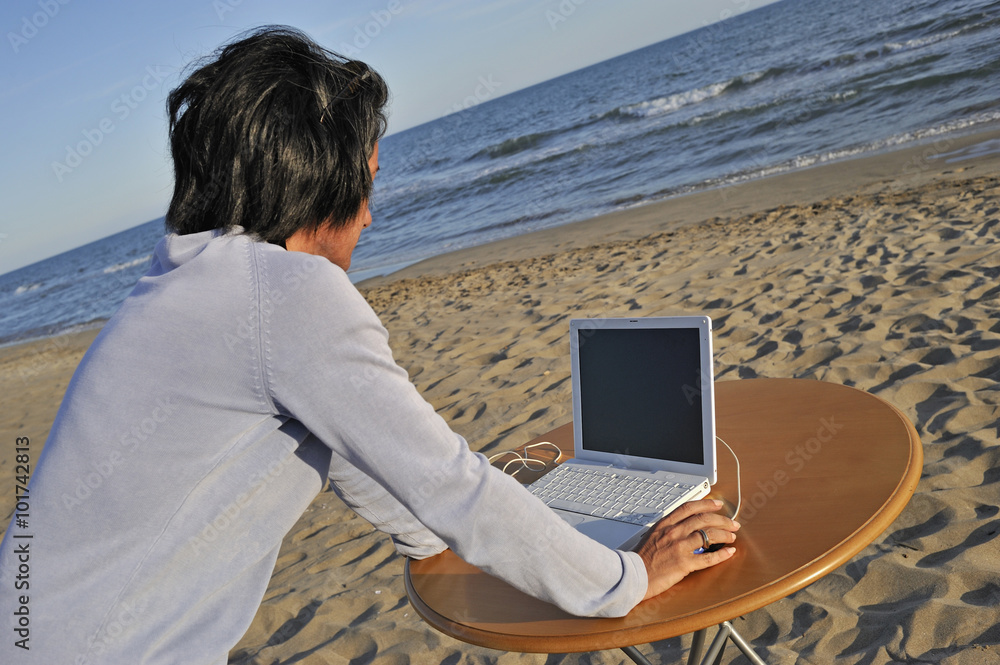 Mid-adult woman using a laptop on the beach