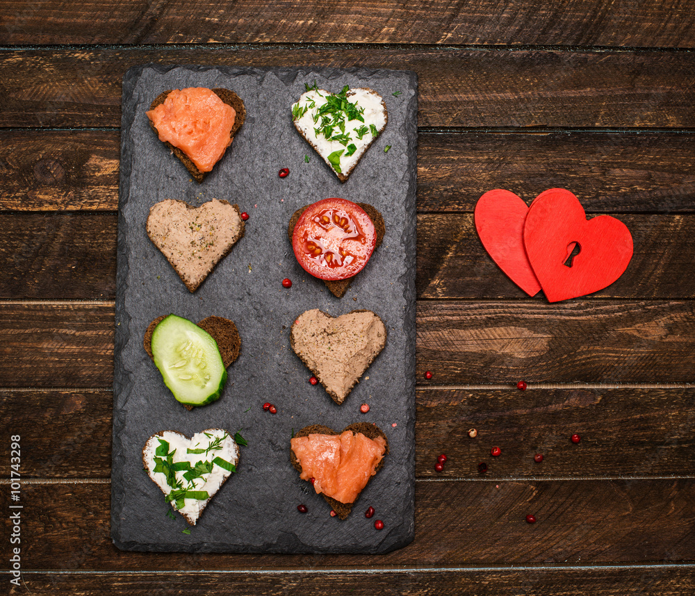 Canapes heart shape with different toppings on black slate board Canapes heart shape with different toppings on black slate board